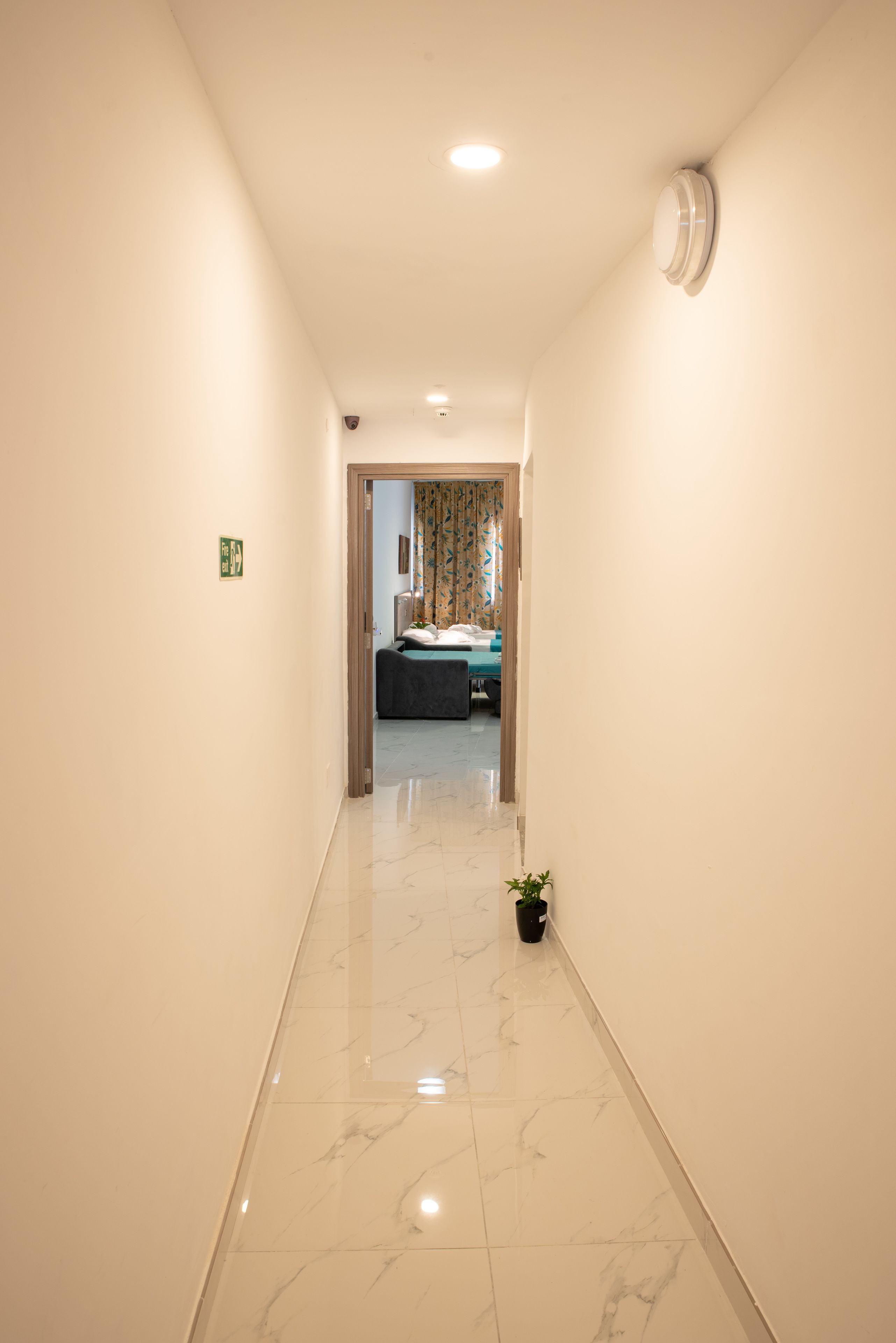 A hallway with a marble floor leading to a room with a bed and curtains.