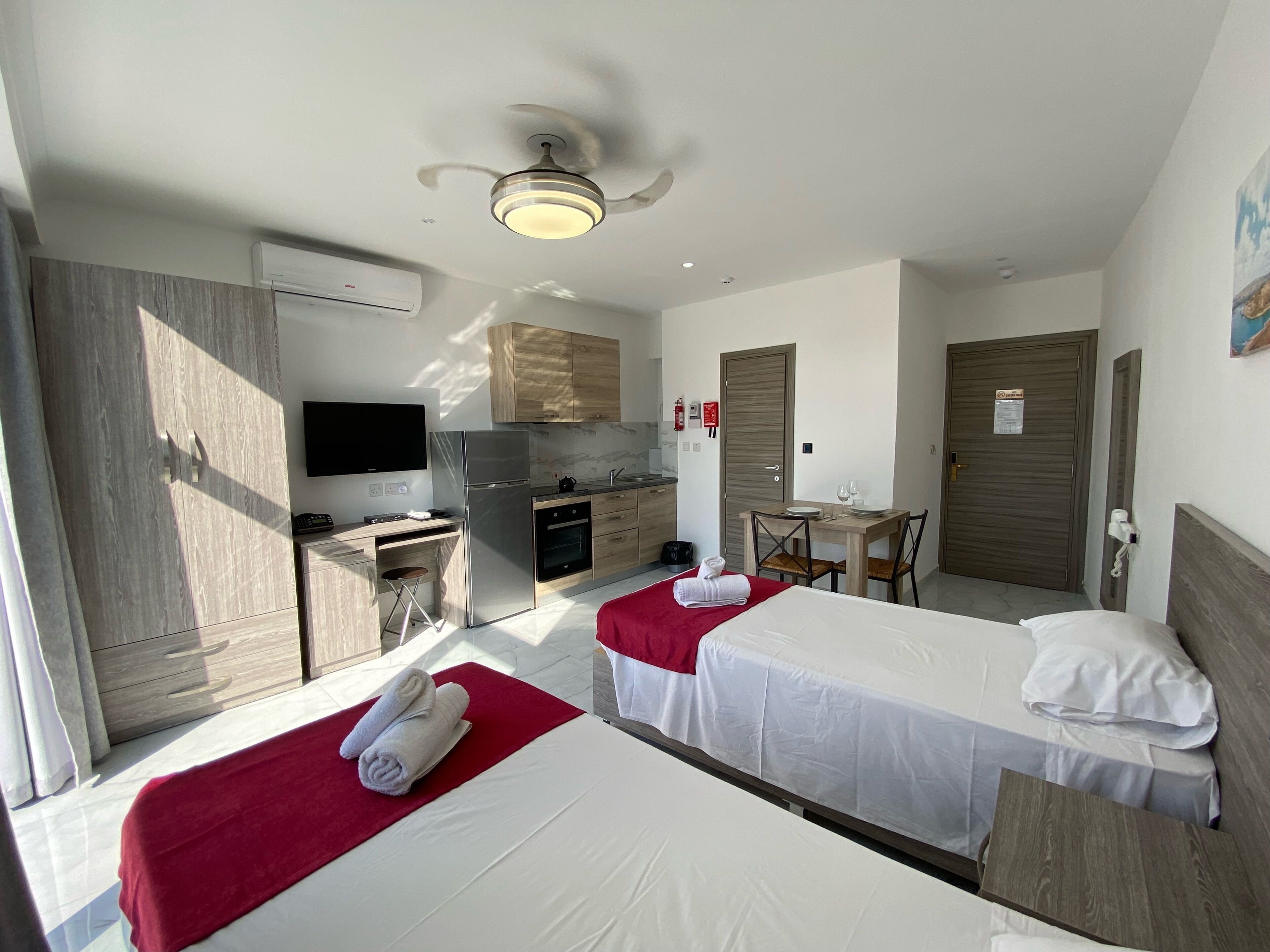 A hotel room with two beds, a kitchenette, a dining area, and a TV.