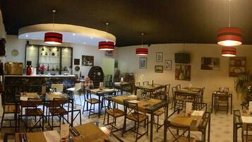 A restaurant with multiple tables and chairs, a bar area, and hanging red lamps.