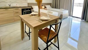 A modern hotel room with a dining area, kitchenette, and a large bed with a balcony. - For Rest Aparthotel (St. Paul's Bay)