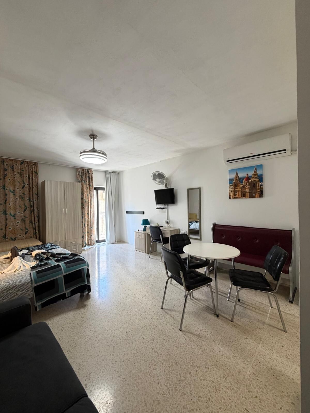 A modern living room with a sofa, a dining table with chairs, a TV, and a painting on the wall.