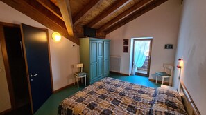 A bedroom with a bed, a wardrobe, two chairs, a radiator, and a door leading to an outside area. - Martinella (Folgaria)