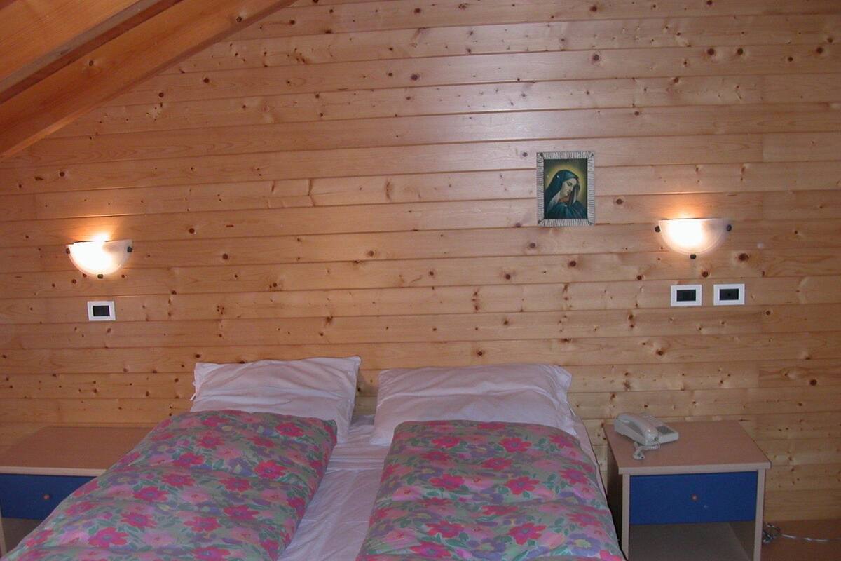 A wooden-paneled room with two beds, each with a floral bedspread. There are wall-mounted lights and a small portrait above the beds.
