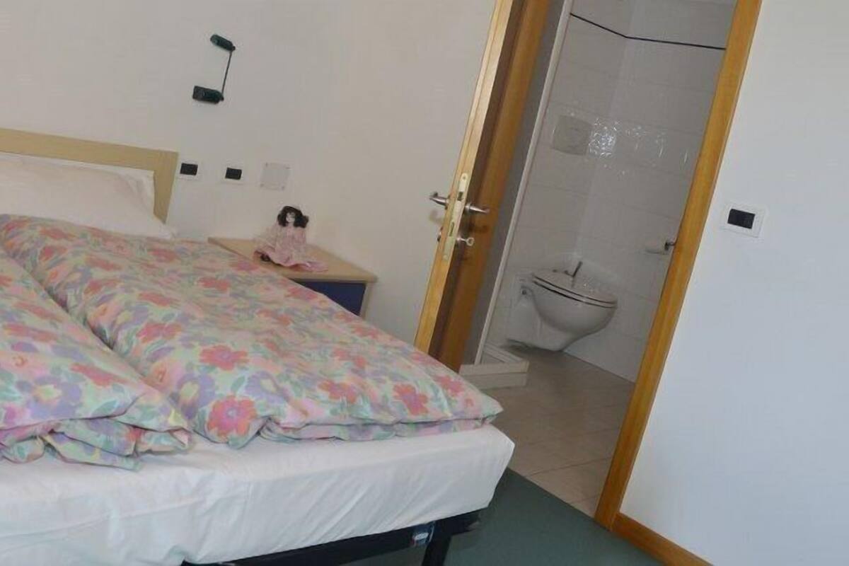 A bedroom with a bed, a nightstand, a doll, and a bathroom visible through an open door.