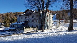 A multi-story building with a snow-covered roof, situated in a snowy landscape with trees and a clear sky. - Martinella (Folgaria)