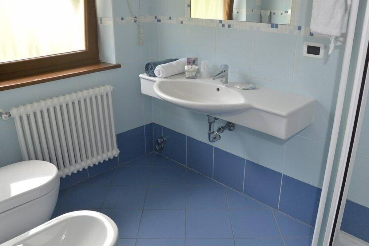 A bathroom with a white sink, blue tiles, a white toilet, and a window.