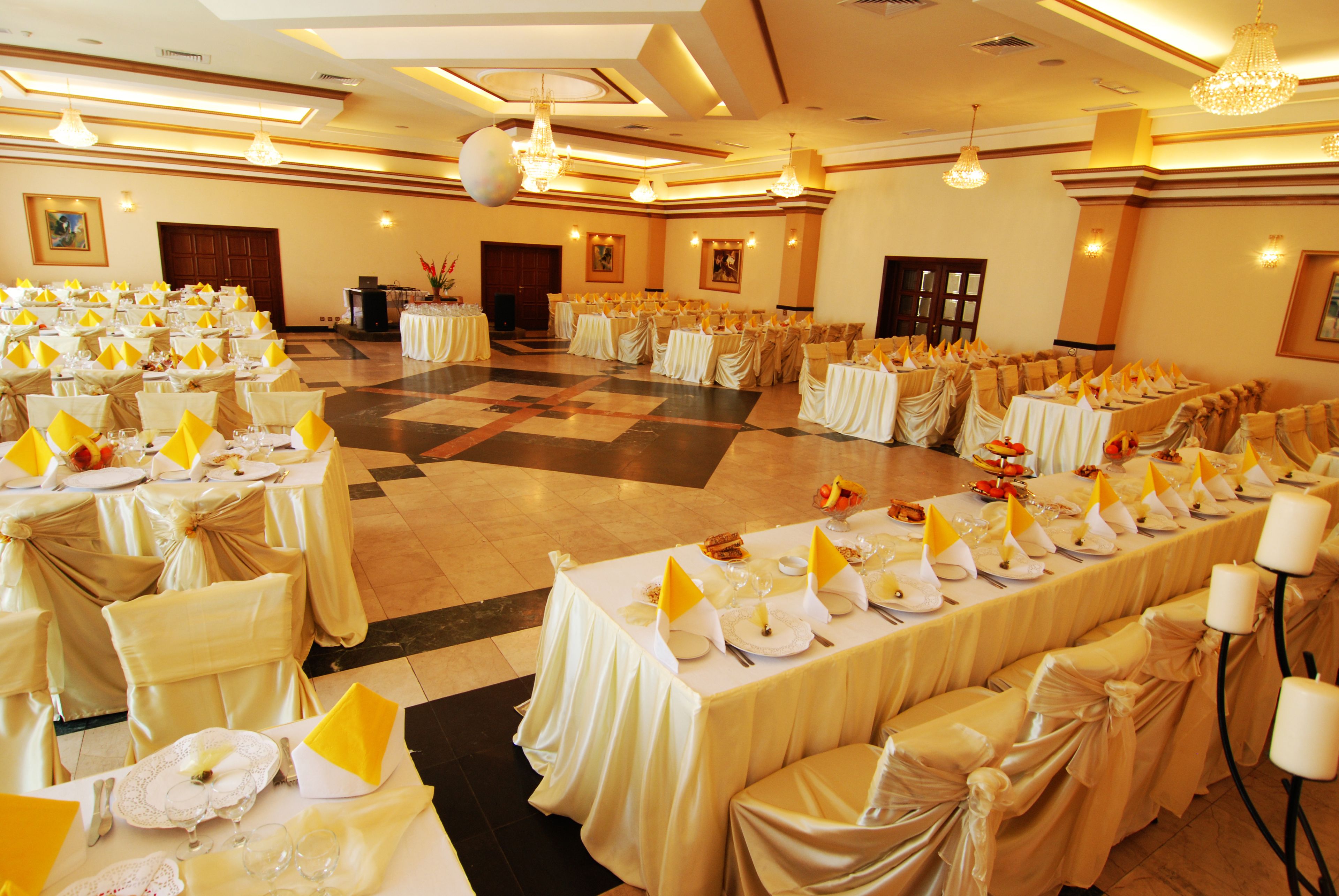 Een banketzaal met rijen tafels gedekt voor een formeel evenement, met witte tafelkleden en gele servetten.