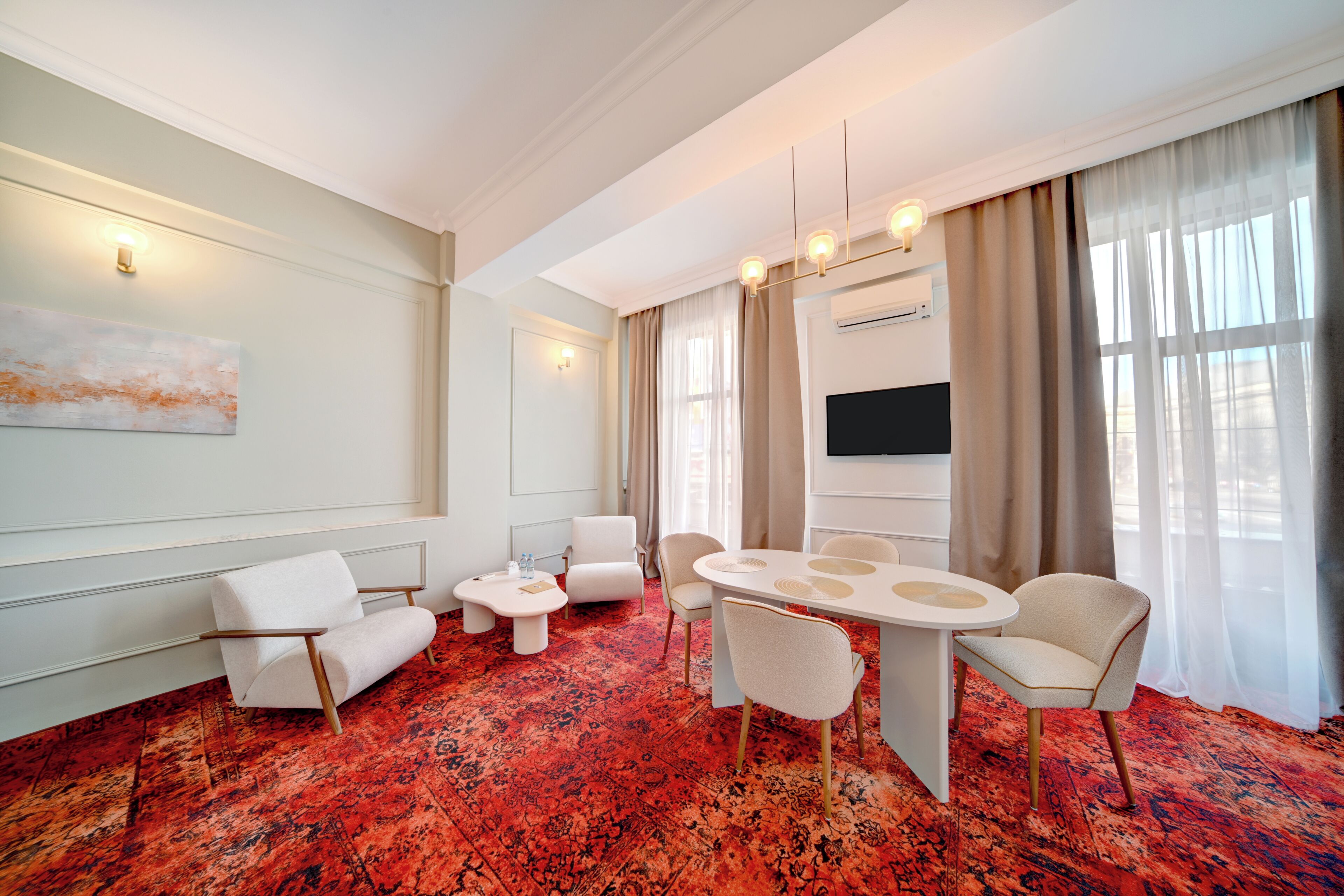 Una camera d'hotel moderna con tappeto rosso, arredi bianchi, televisore a schermo piatto e una grande finestra con tende.