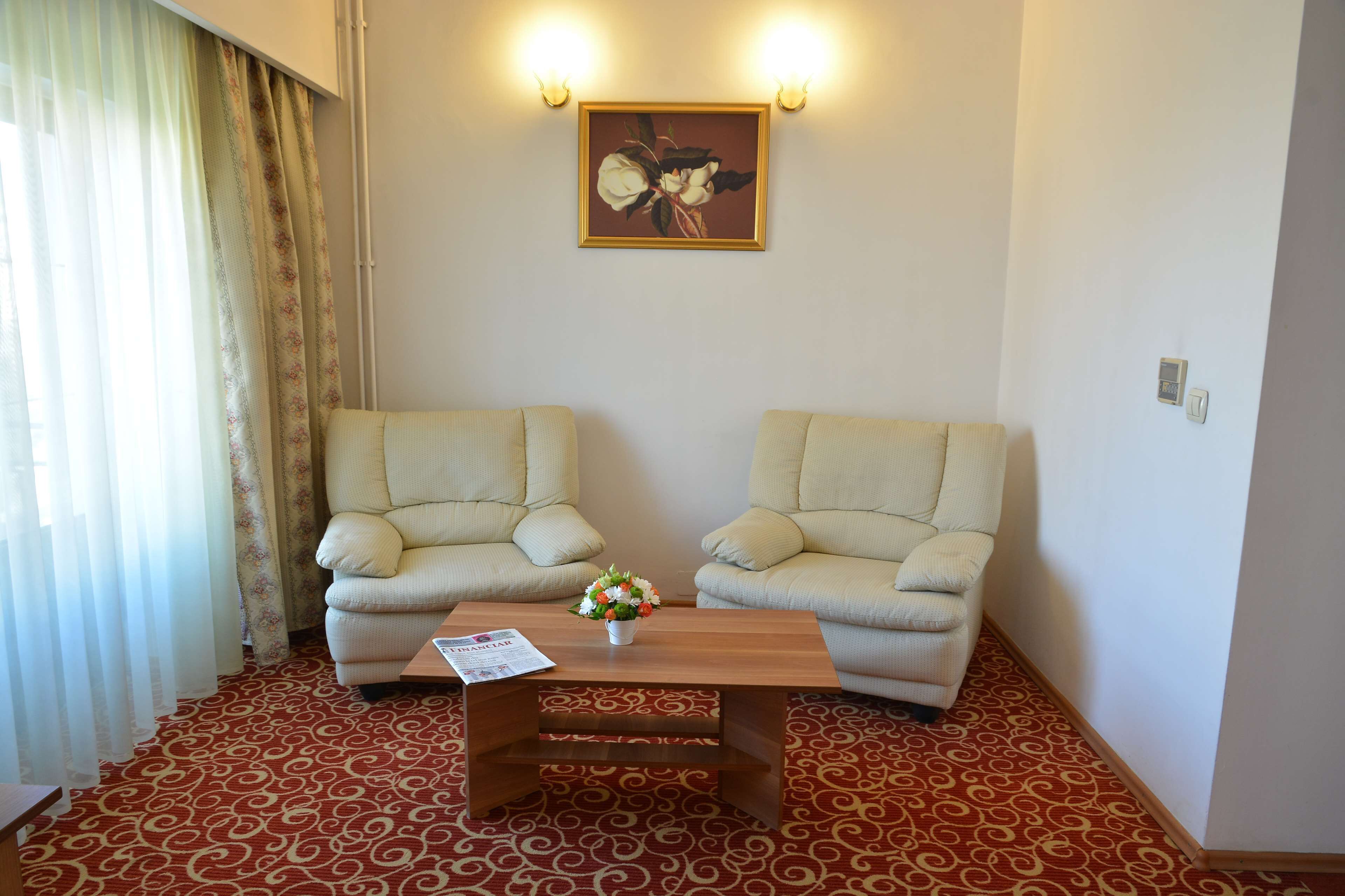 A room with two beige armchairs, a wooden coffee table with a floral vase, and a painting on the wall.