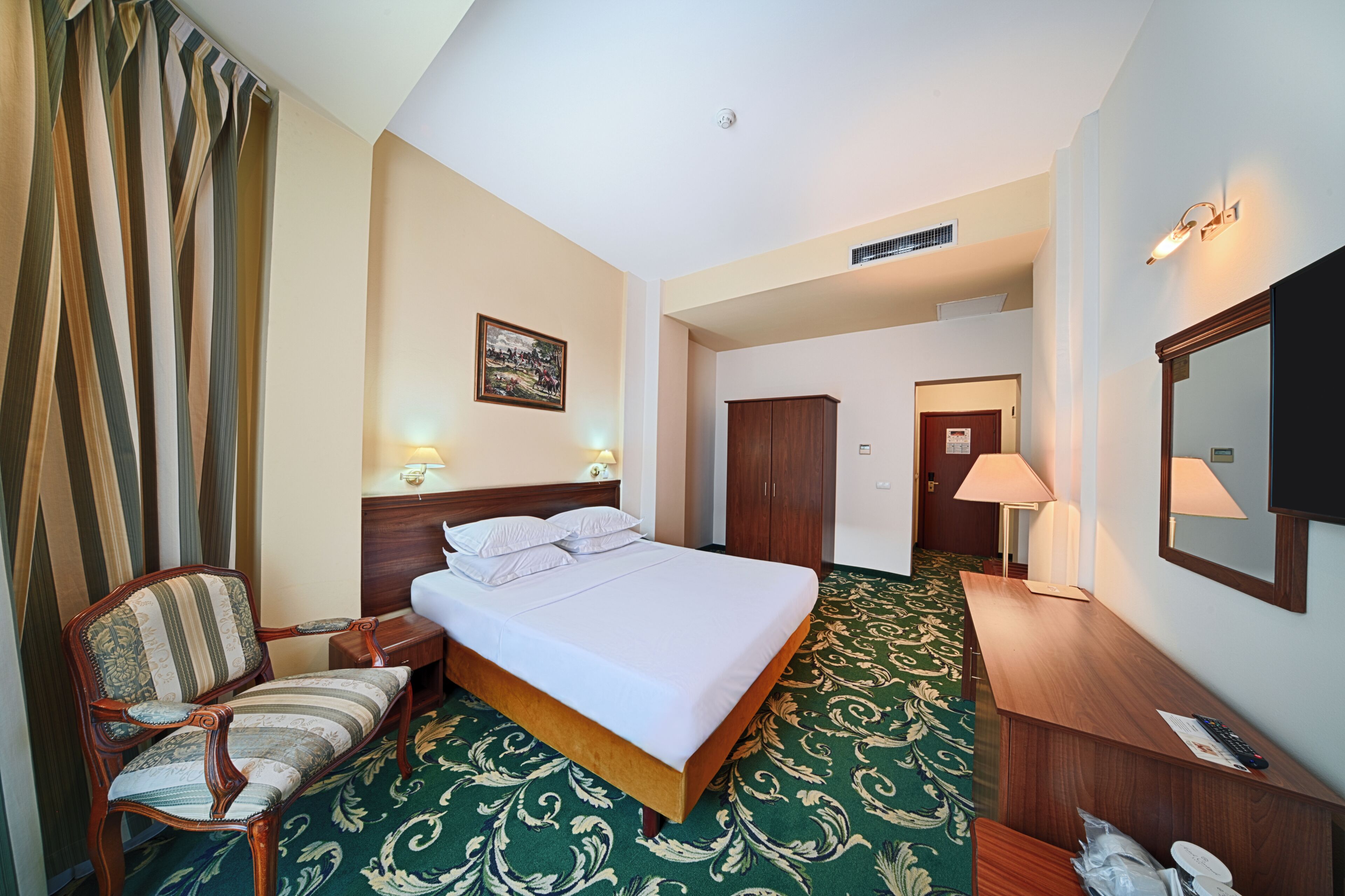Ein Hotelzimmer mit Bett, Stuhl, Schreibtisch, Spiegel und Tür.