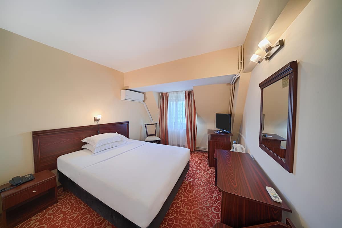 Habitación de hotel con una cama grande, un escritorio, una silla, un espejo y una ventana con cortinas.