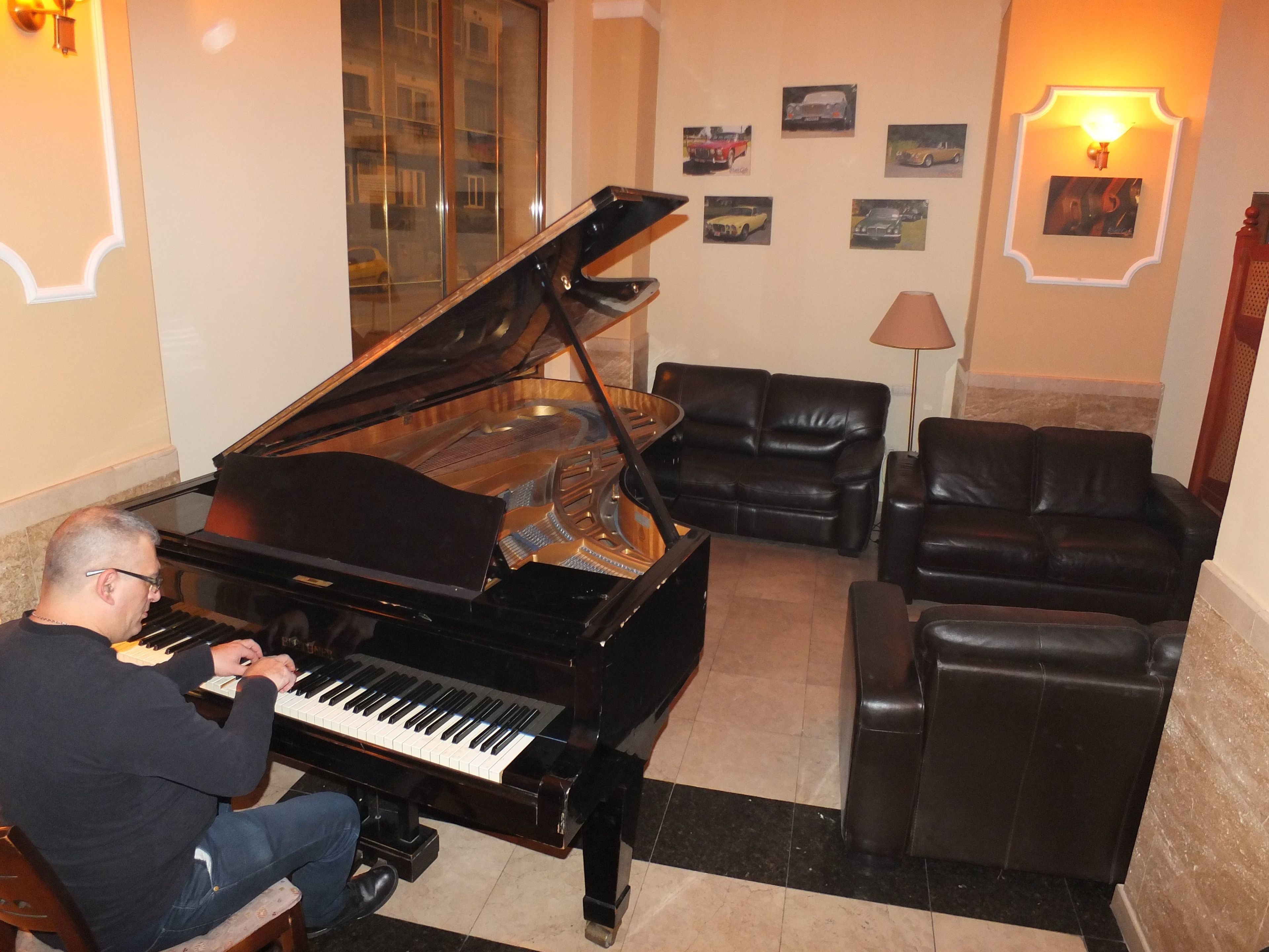 A grand piano in a well-lit room with a sofa and a lamp.