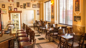 Un restaurante con varias mesas y sillas, una barra con vitrina y cuadros en las paredes.