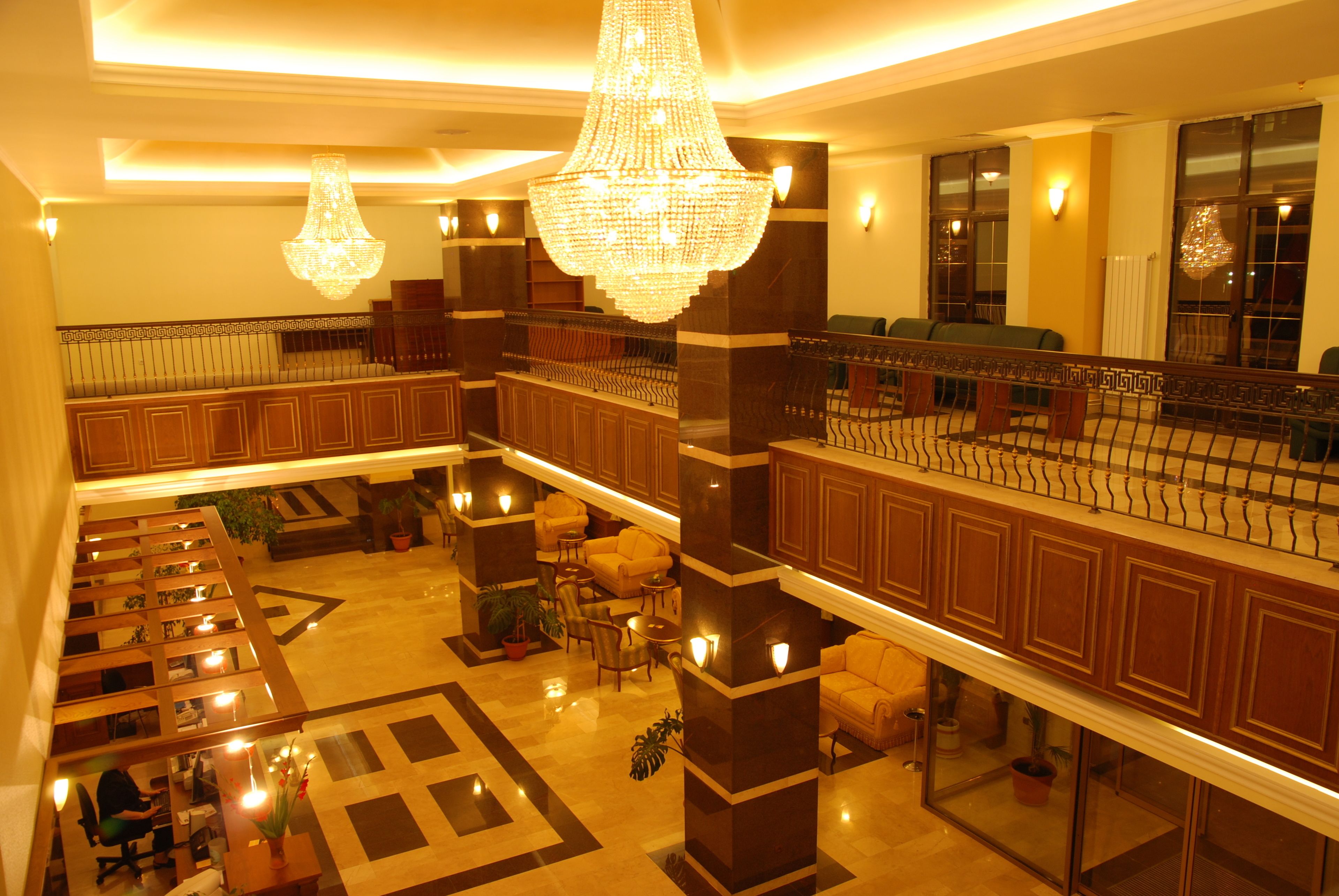 A spacious lobby with a grand chandelier, multiple seating areas, and a staircase leading to an upper level.