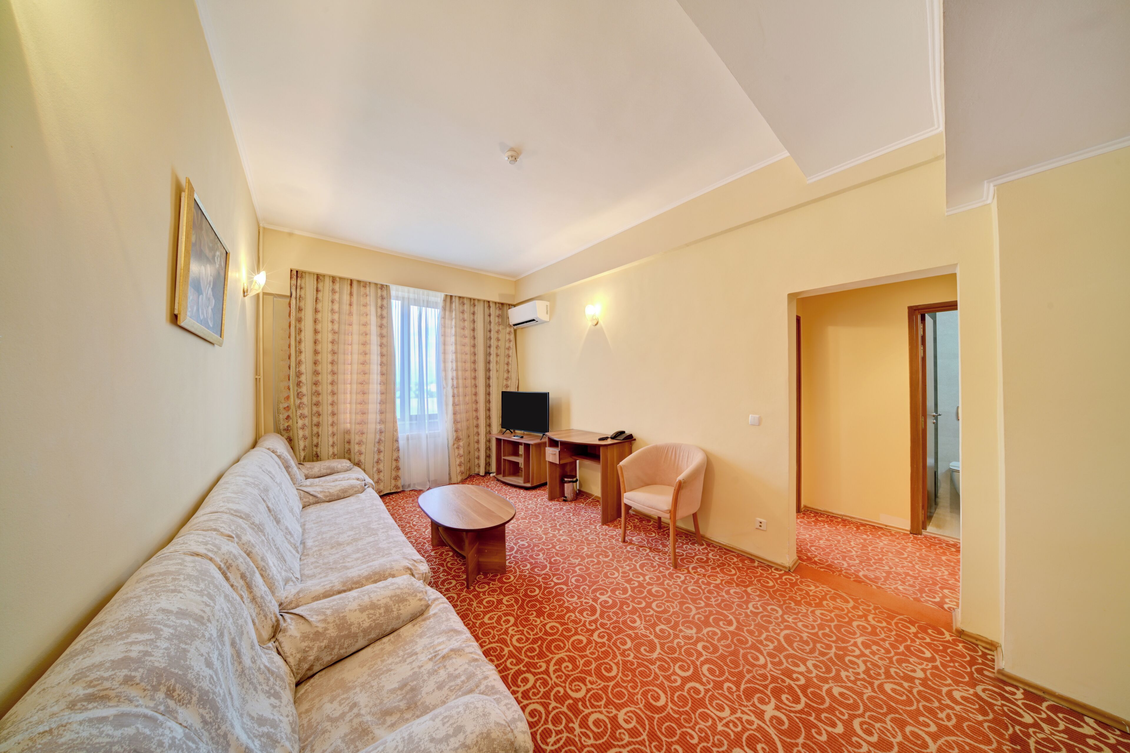 Habitación de hotel con sofá, una mesita, televisión y escritorio.