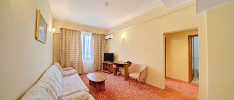 Habitación de hotel con sofá, una mesita, televisión y escritorio.