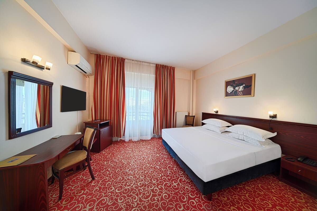 Habitación de hotel con cama, escritorio, silla, televisor y un cuadro en la pared.