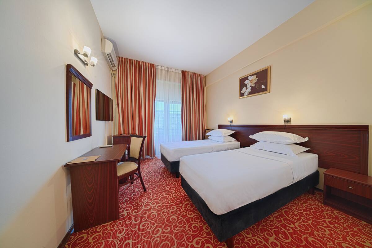 Habitación de hotel con dos camas, un escritorio, una silla, una mesita de noche y un cuadro en la pared.