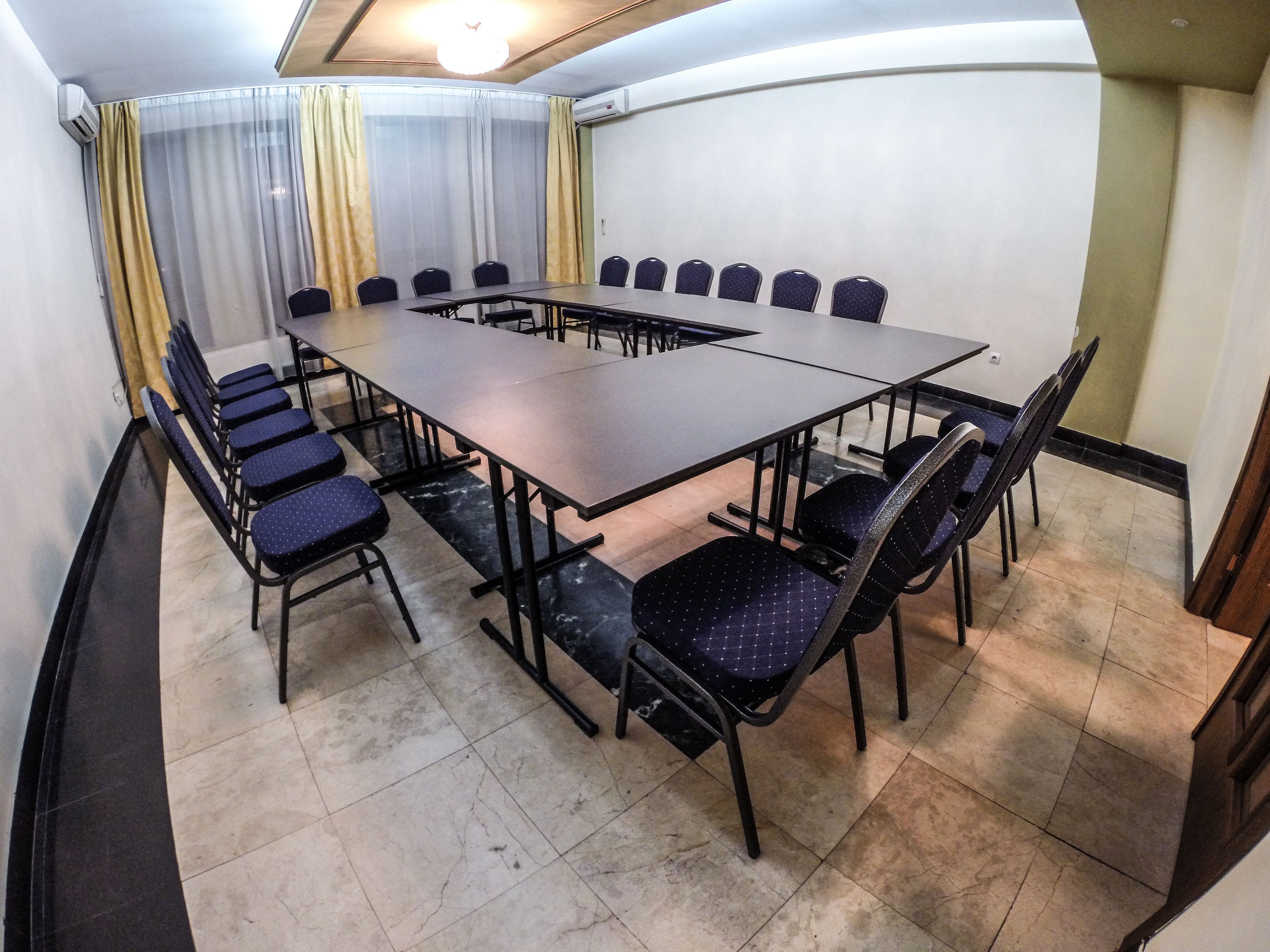 A conference room with a long table and chairs, air conditioning, and curtains.