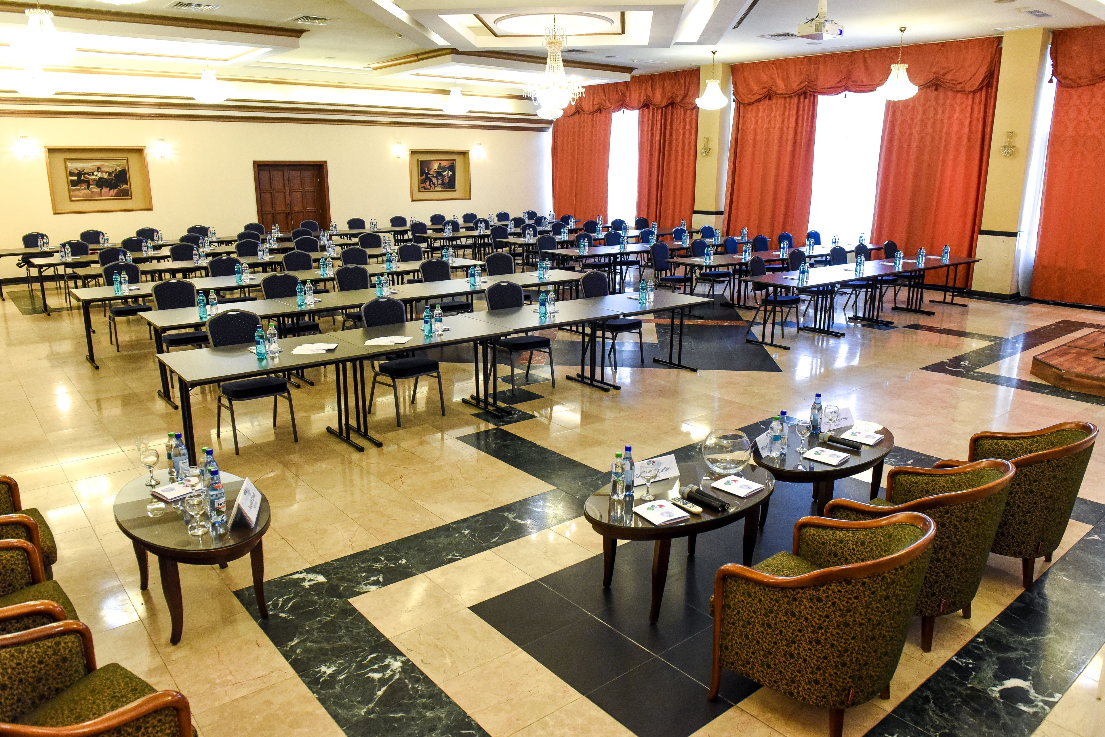 Un salón de conferencias con varias mesas, sillas y botellas de agua.