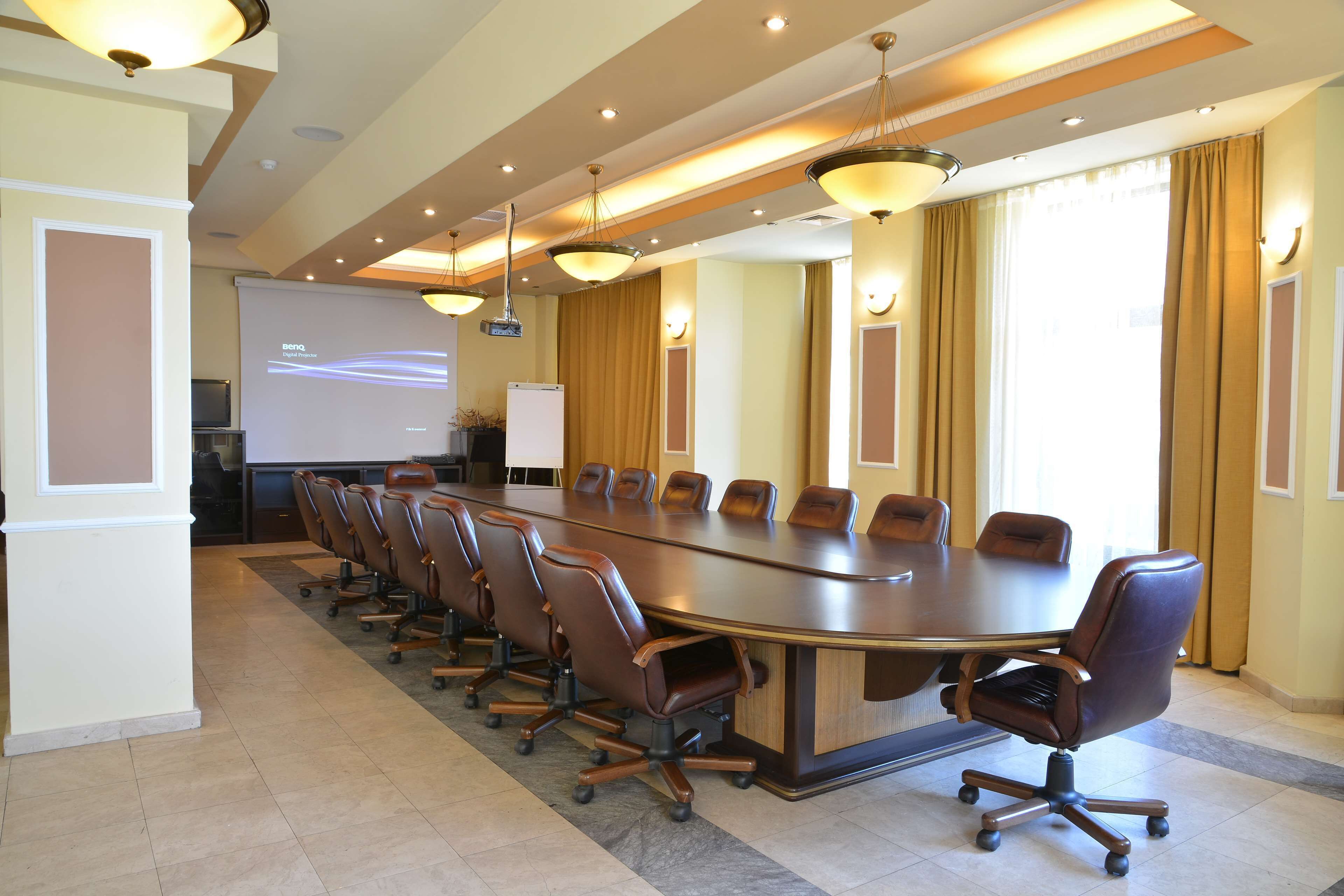 A conference room with a long table, multiple chairs, a projector screen, and a presentation on the wall.