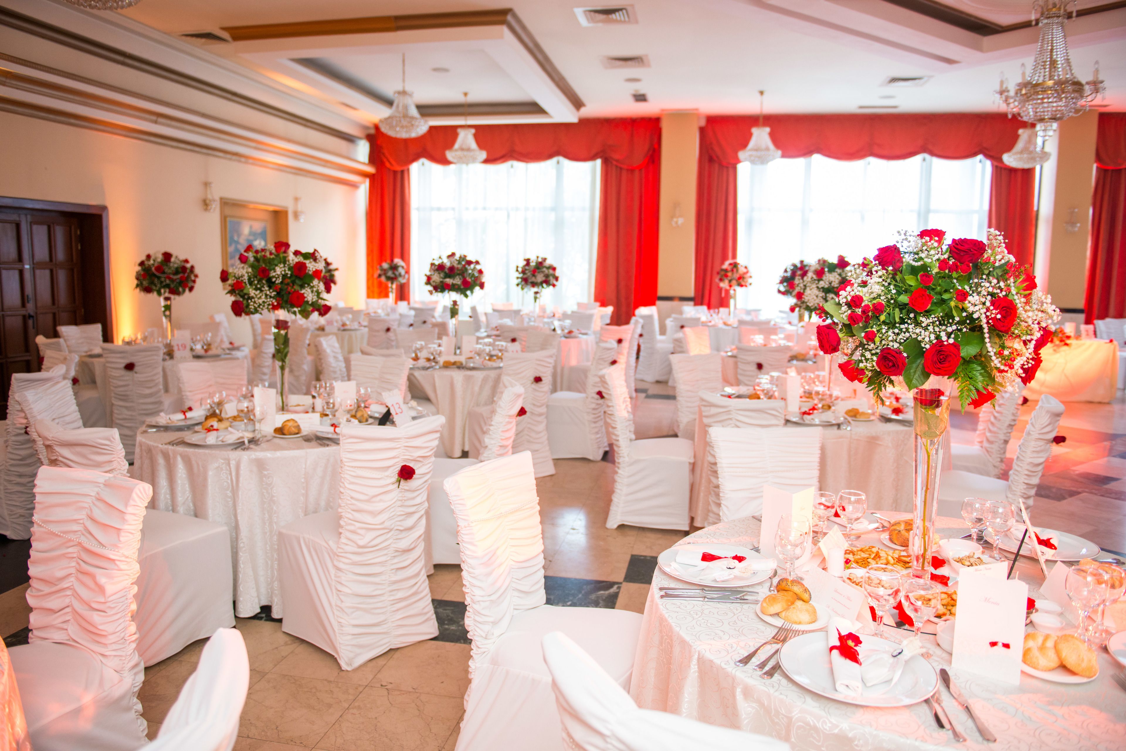 Un salón de banquetes con mesas redondas dispuestas para un evento formal, manteles blancos y centros de mesa florales.