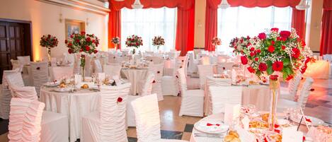 Un salón de banquetes con mesas redondas dispuestas para un evento formal, manteles blancos y centros de mesa florales.