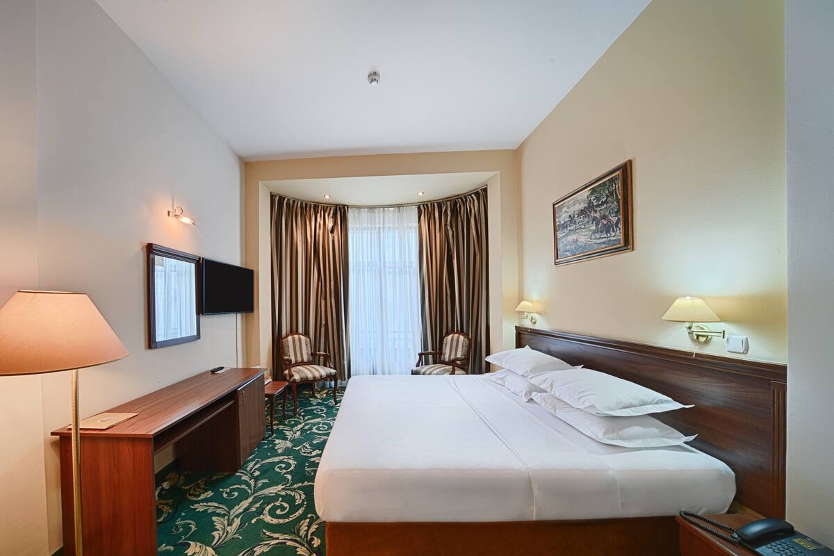 Habitación de hotel con una cama grande, un escritorio con lámpara, una silla, un televisor y un cuadro en la pared.
