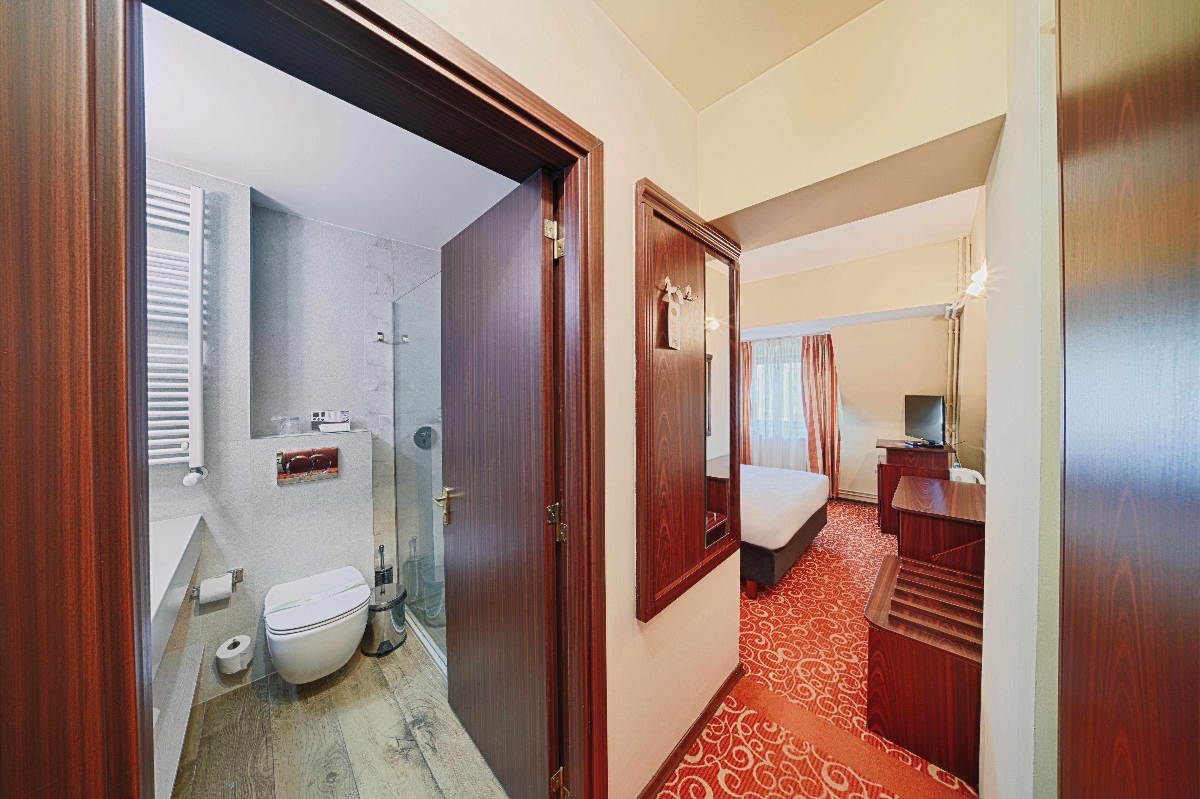Una habitación de hotel con baño, cama, escritorio y espejo.