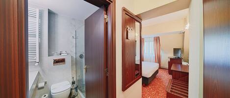 Una habitación de hotel con baño, cama, escritorio y espejo.