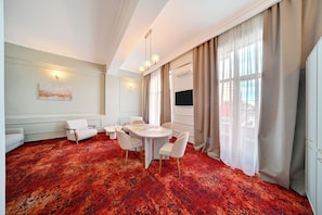 A hotel room with a red carpet, a round table with chairs, a sofa, a TV, and a large window with curtains. - Central Hotel (Ploiesti)