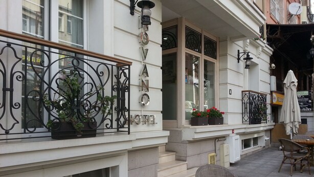 Een hotelgevel met een balkon, terrasstoelen en een bord.