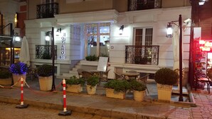 Een hotel met een klassiek gevelontwerp, een terras met plantenbakken en een zichtbare trap naar de ingang.