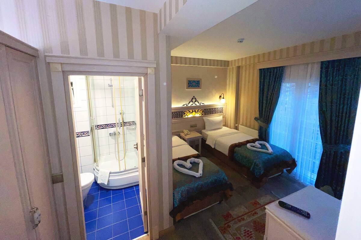 A hotel room with a shower, two beds, a small table, and a TV.