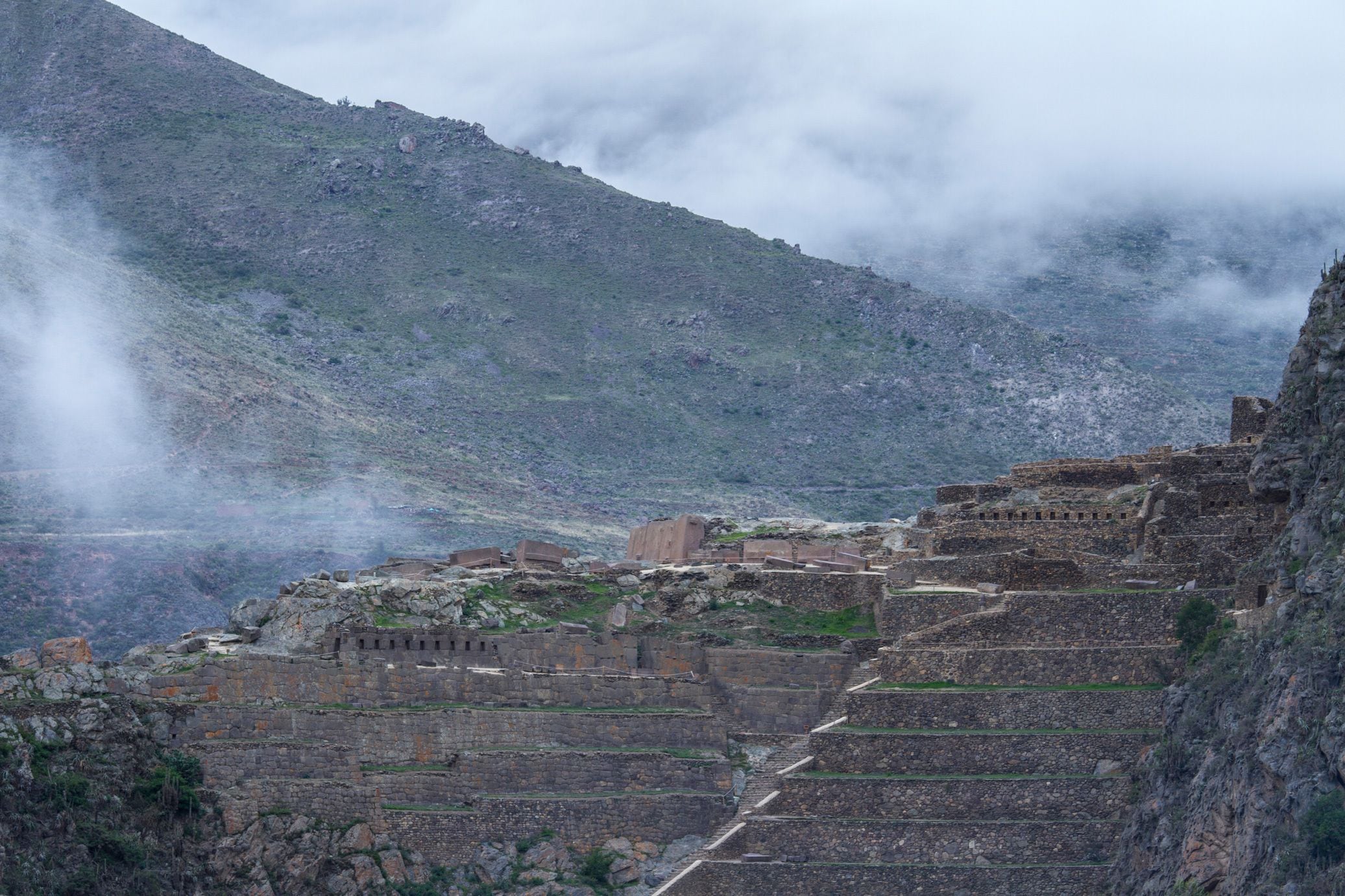 Una ciudad antigua en terrazas con estructuras de piedra y un telón de fondo montañoso.