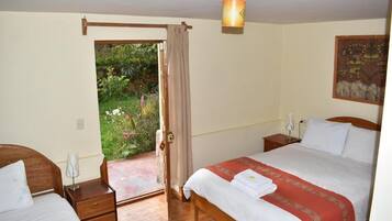 Quarto com duas camas, piso de madeira, porta que dá para um jardim e uma luminária fixada na parede.