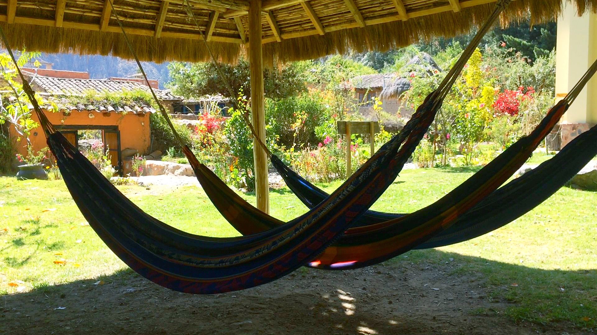 Una hamaca bajo una estructura de techo de paja en un jardín, con vistas a edificios tradicionales.