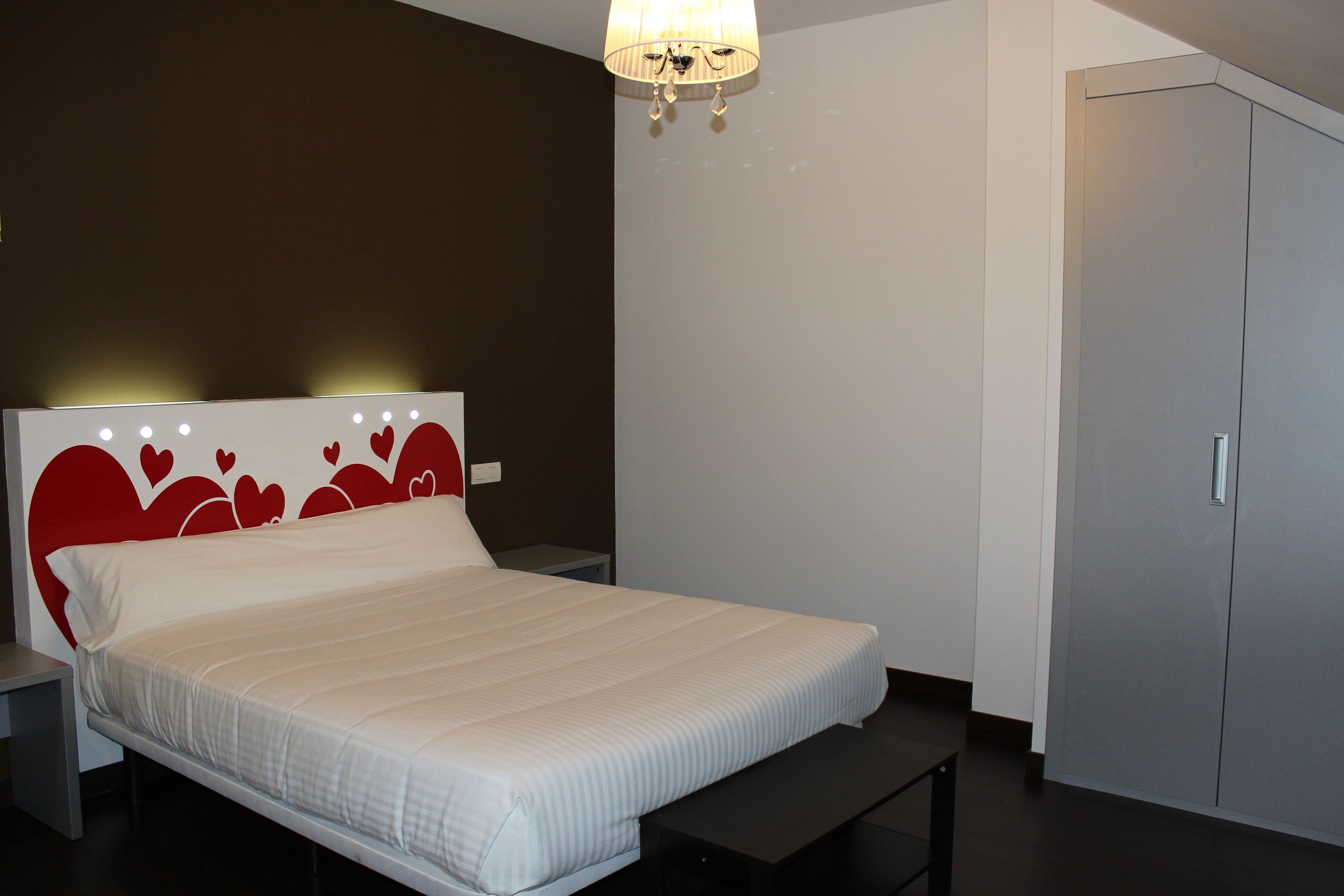 A bedroom with a bed, bedside tables, a bench, a wardrobe, and a chandelier.