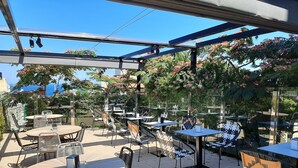 An outdoor patio with tables and chairs, surrounded by greenery and a clear blue sky. - Calas de Liencres (Pielagos)