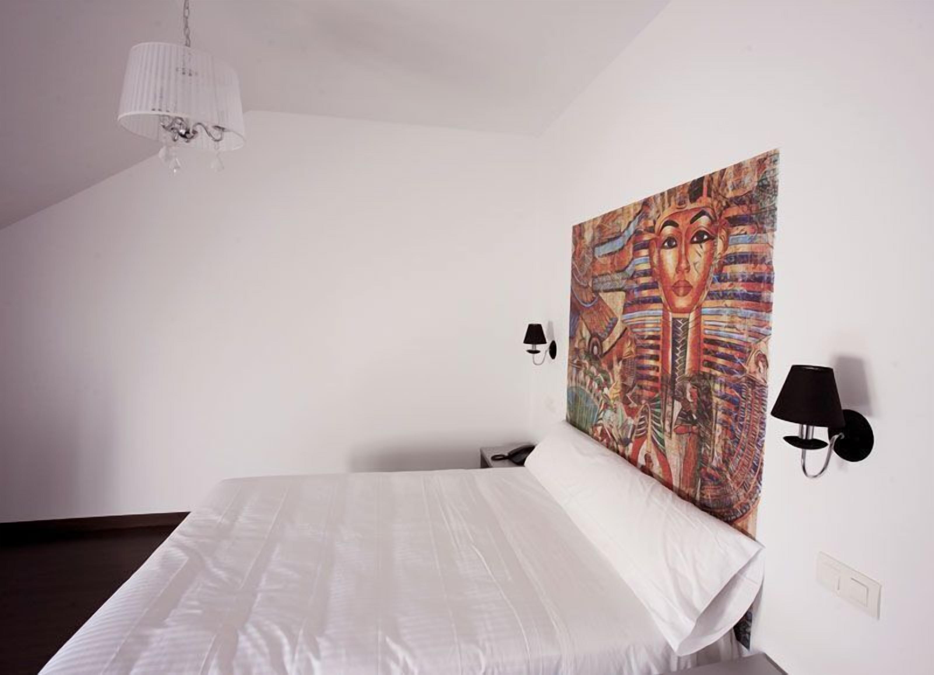 Camera d'albergo con un letto grande, un lampadario, due lampade a parete e un arazzo colorato.