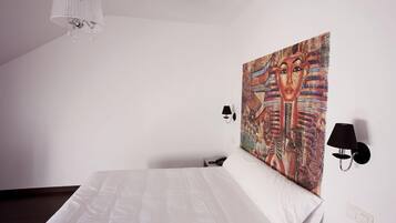 A hotel room with a large bed, a chandelier, two wall-mounted lamps, and a colorful tapestry on the wall.