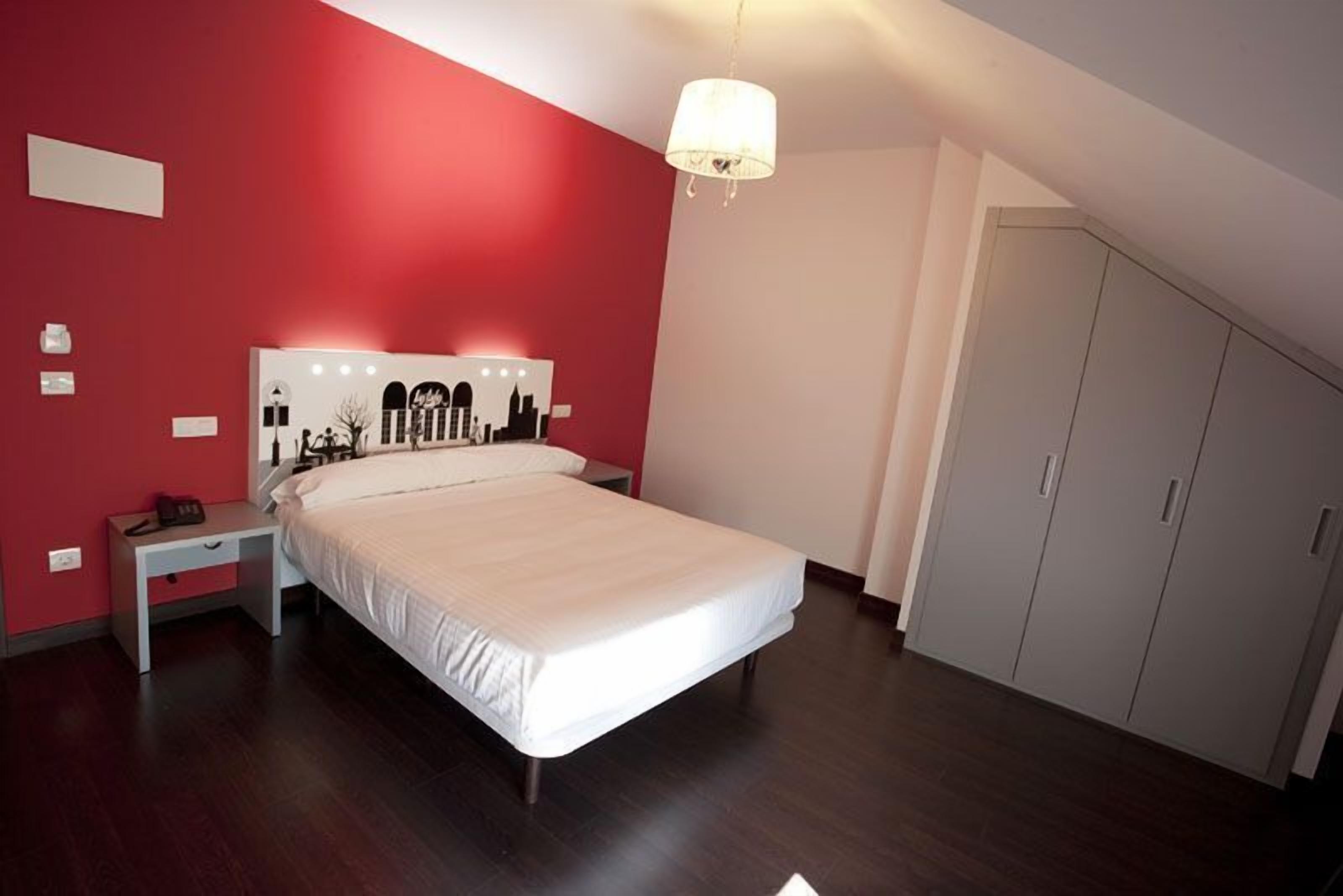 A bedroom with a bed, a nightstand, a wardrobe, and a cityscape artwork on the wall.