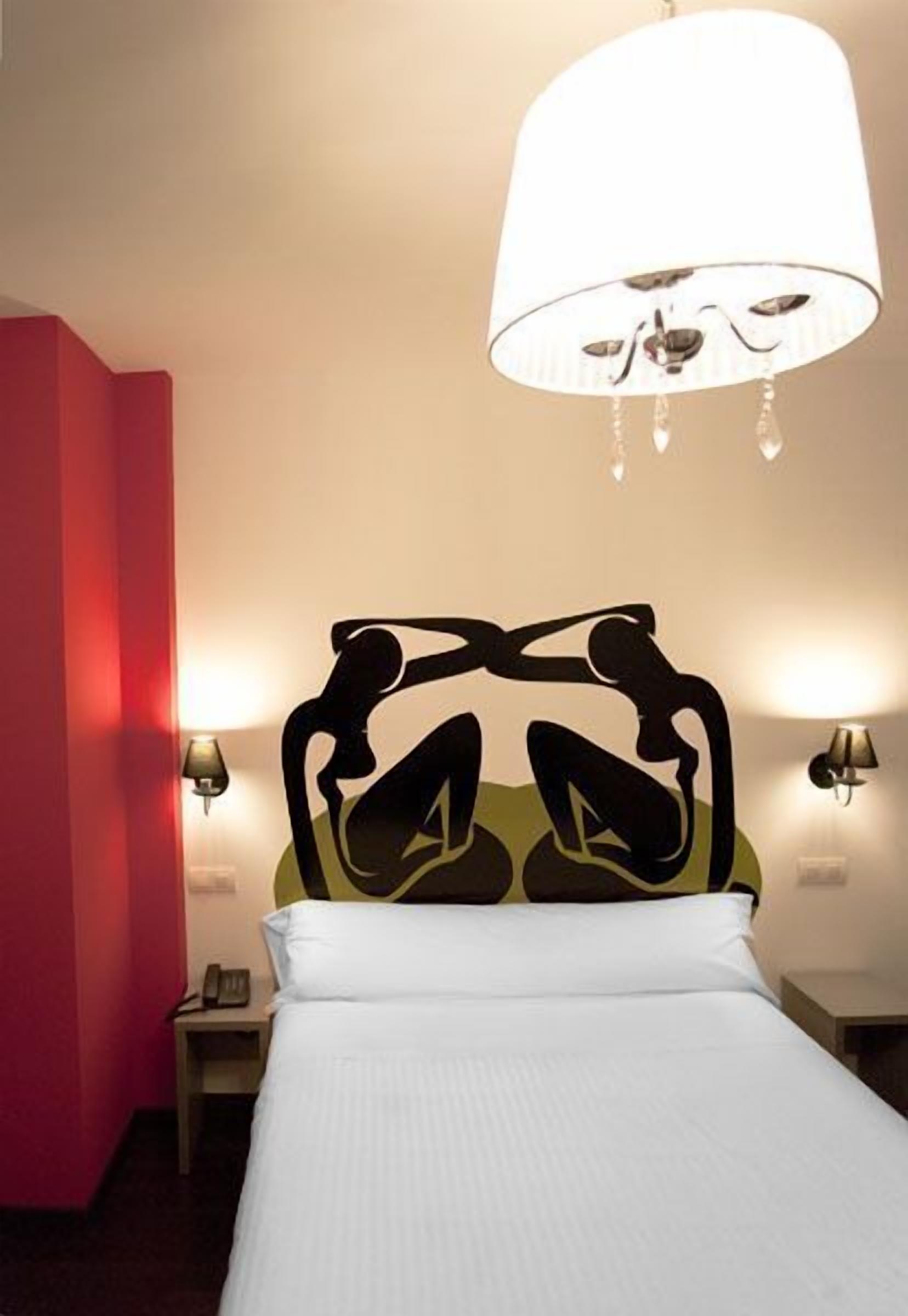 A hotel room with a bed, a chandelier, and wall-mounted lamps.