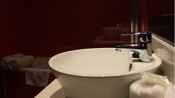 Un lavamanos blanco con grifo cromado en un baño con paredes de azulejos rojos.