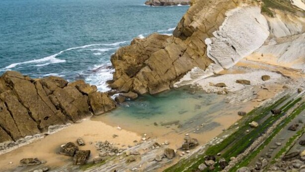 A coastal landscape with rocky cliffs, a sandy beach, and a clear view of the sea. - Calas de Liencres (Pielagos)