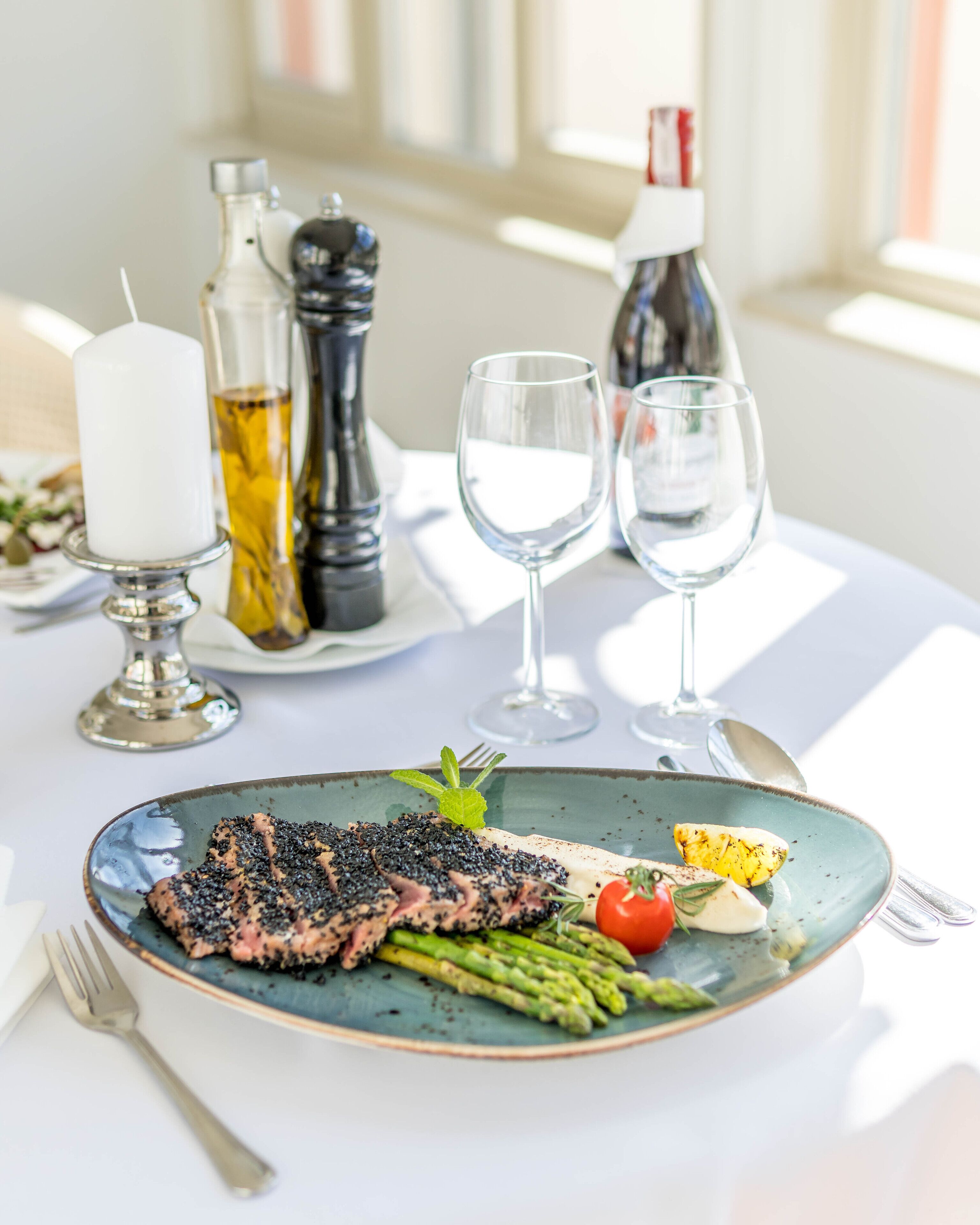 Une table à manger avec une assiette de nourriture, comprenant du poisson grillé et des asperges, ainsi qu’une bougie.