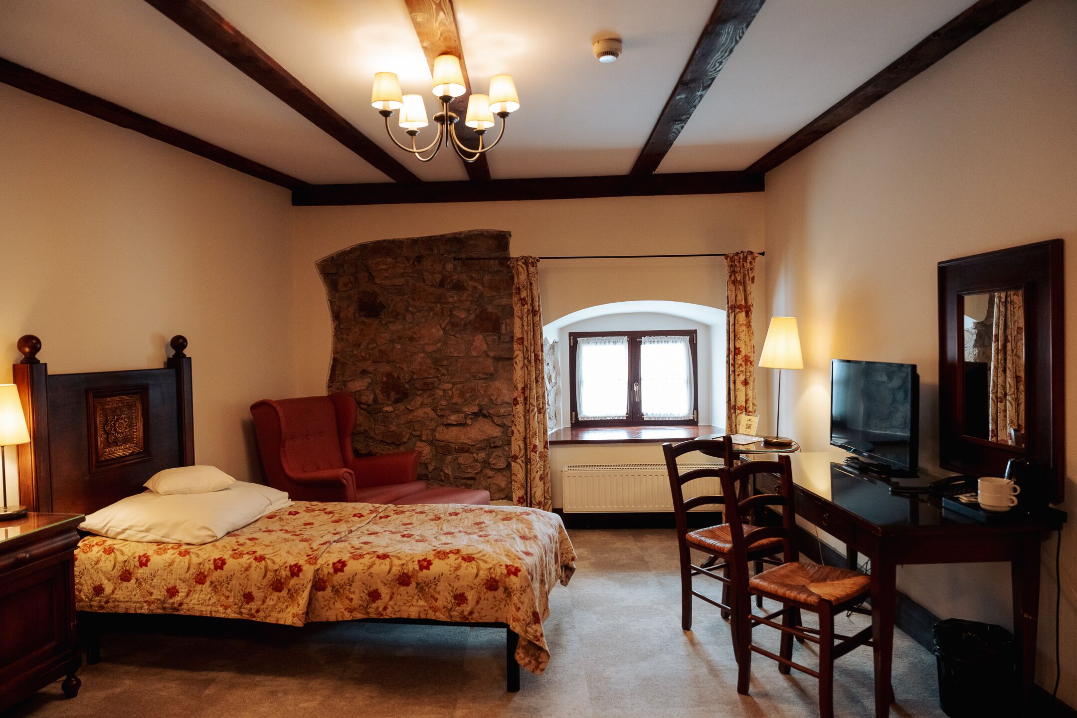 A bedroom with a bed, a desk, a chair, a television, and a stone wall.