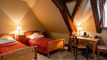 A room with two wooden beds, a desk, and a chair, with a sloped ceiling and exposed wooden beams.