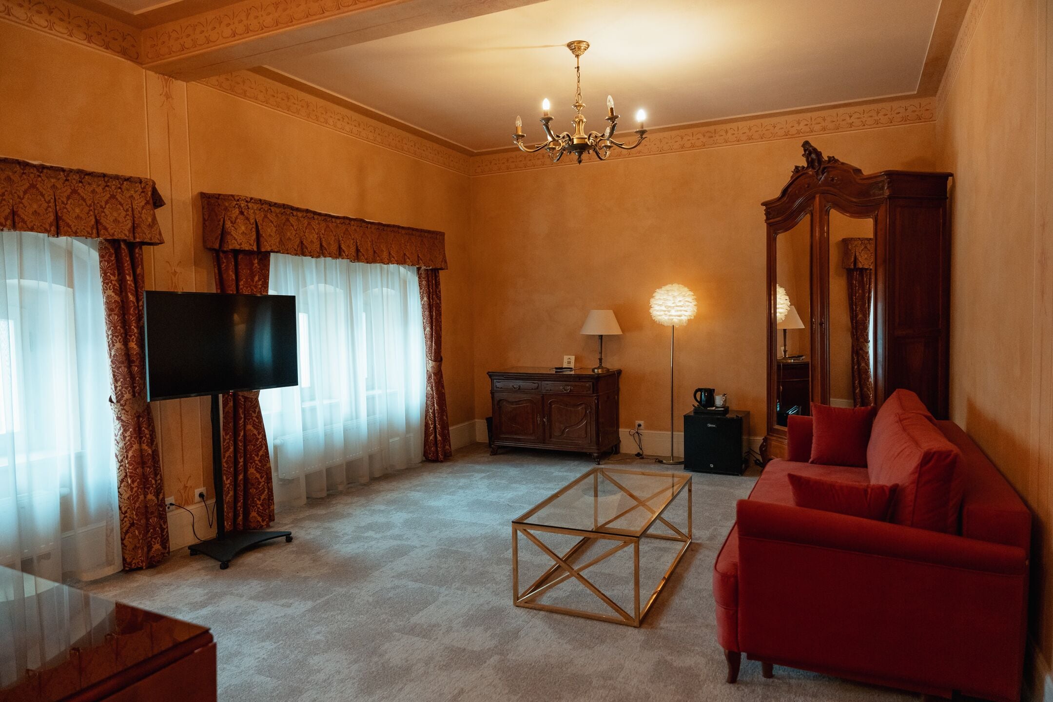 A living room with a TV, red sofa, glass coffee table, and a chandelier.