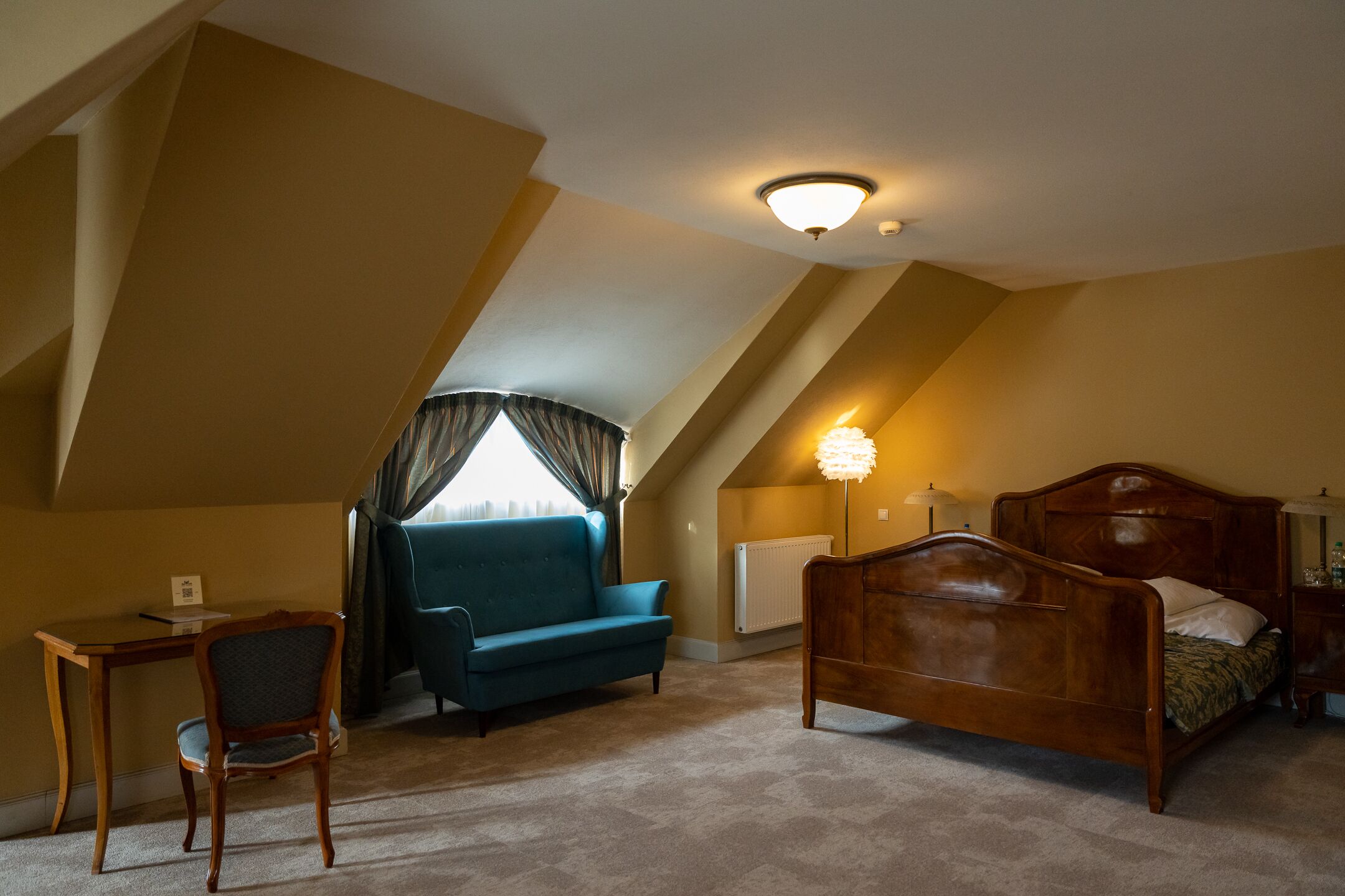A bedroom with a wooden bed, a blue sofa, a desk, and a chair.